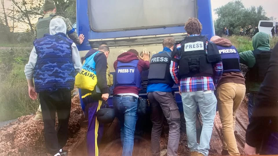En gruppe af journalister iført presseveste skubber en bus fri af mudderet.